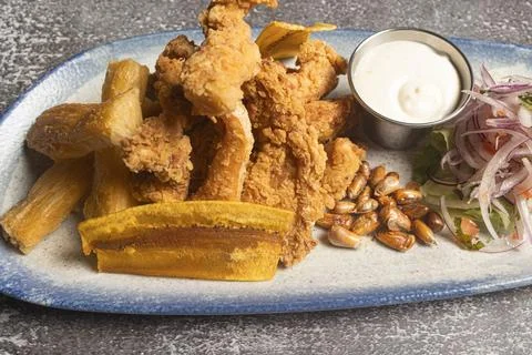 Breaded chicken strips served with fried yucca, plantain, cancha, salad and.. Stock Photos