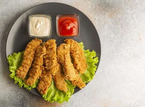 Breaded chicken strips with two kinds of sauces on gray plate. Fast food on gray Stock Photos