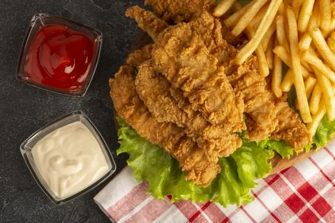 Breaded chicken strips with two kinds of sauces and fried potatoes on a stone Stock Photos