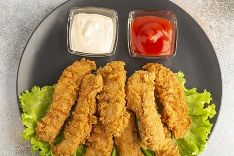 Breaded chicken strips with two kinds of sauces on gray plate. Fast food on gray Stock Photos