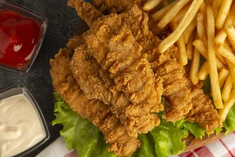Breaded chicken strips with two kinds of sauces and fried potatoes on a stone Stock Photos