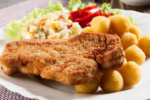 Breaded chop, prepared potatoes and salad. mysterious light. Stock Photos