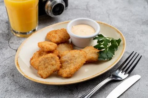 Breaded crispy chicken nuggets with cheese sauce on grey table, served with o Stock Photos