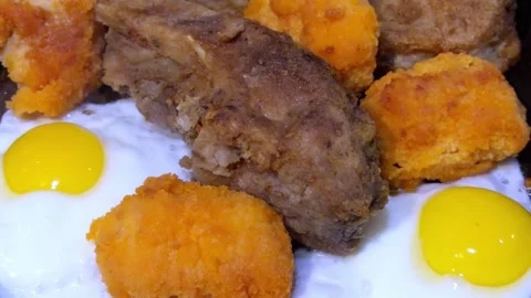 Breaded fish pieces and fried eggs in close up in the pan Video stock 324520566