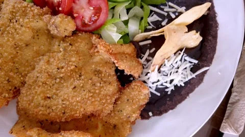 Breaded fried cutlet served with black beans and fresh salad Video stock 328702408