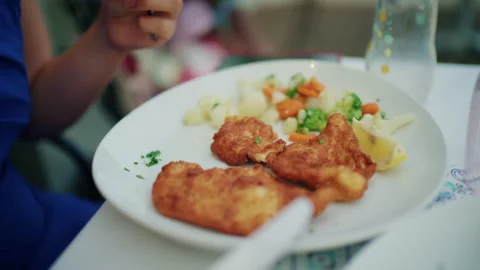 Breaded schnitzel with cauliflower, broccoli and carrots as hands cut the meat Vidéo 348104994