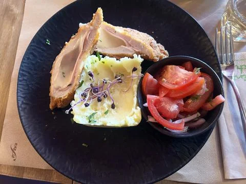 Breaded stuffed chicken cordon bleu with mashed potatoes and tomato salad plate Stock Photos