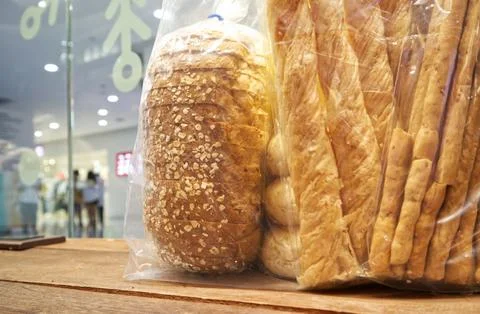 Breadsticks and loaves of bread in plastic bags were placed on the wooden table Fotos de archivo