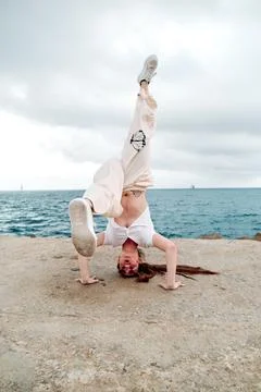 Breakdance dancer doing a handstand outdoors near the sea. Stock Photos