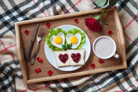 Breakfast in bed with heart-shaped eggs, toasts, jam, coffee, rose and petals Stock Photos