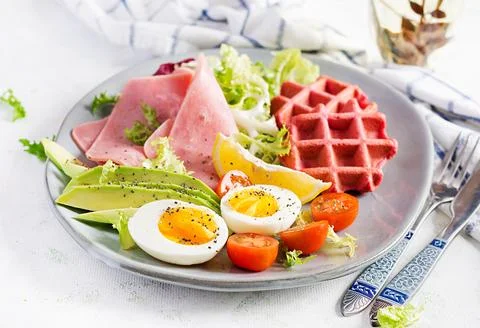 Breakfast with beetroot waffles, boiled egg, ham, tomato and slice avocado .. Stock Photos