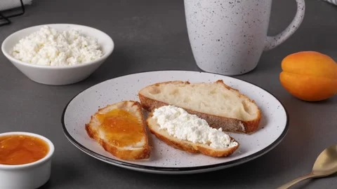 Breakfast with bread, cottage cheese, jam, and a drink on a simple table Vídeos de archivo 340962453