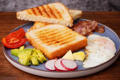 Breakfast bread with fried egg, bacon, pepper, avocado, tomato p Stock Photos