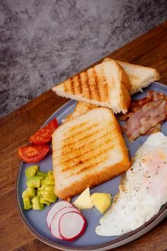 Breakfast bread with fried egg, bacon, pepper, avocado, tomato p Stock Photos