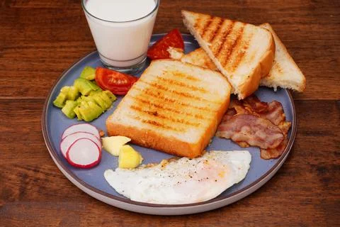Breakfast bread with fried egg, bacon, pepper, avocado, tomato p Stock Photos
