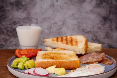 Breakfast bread with fried egg, bacon, pepper, avocado, tomato p Stock Photos