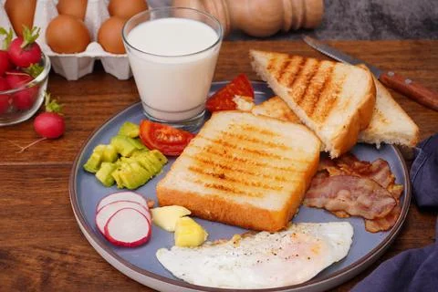 Breakfast bread with fried egg, bacon, pepper, avocado, tomato p Stock Photos