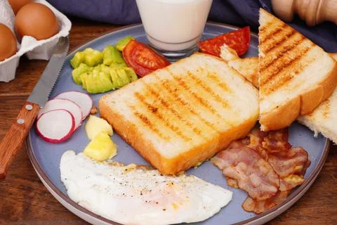 Breakfast bread with fried egg, bacon, pepper, avocado, tomato p Stock Photos