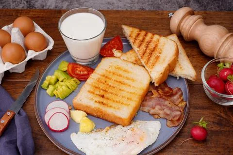 Breakfast bread with fried egg, bacon, pepper, avocado, tomato p Stock Photos