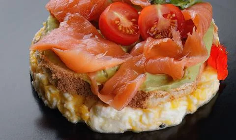 Breakfast, bread toast with scrambled eggs, salmon, avocado and tomatoes Stock Photos