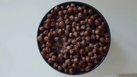 Breakfast cereals in the form of chocolate corn balls in milk on a plate. The Stock-Footage 135363832