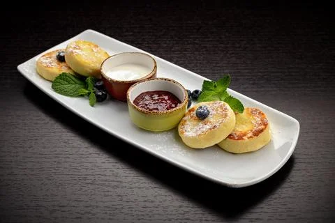 Breakfast, cheesecakes with two sauces. mint and blueberries, on a dark backg Stock Photos