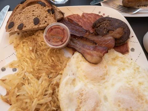 Breakfast consisting of fried eggs, hash browns, meat including ham, bacon,.. Stock Photos