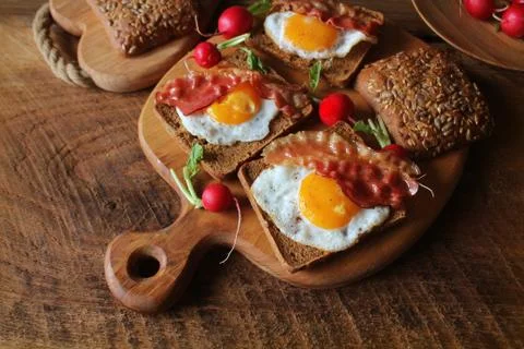 Breakfast of crispy bacon, fried eggs and bread. Sandwiches on cutting board. Stock Photos
