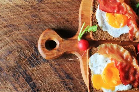 Breakfast of crispy bacon, fried eggs and bread. Sandwiches on cutting board. Foto stock