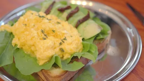 Breakfast dish with scrambled eggs and avocado on toast Stock Footage 345386541