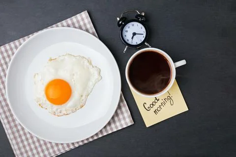 Breakfast featuring a sunny side up egg, a cup of dark coffee, and a note g.. 스톡 사진