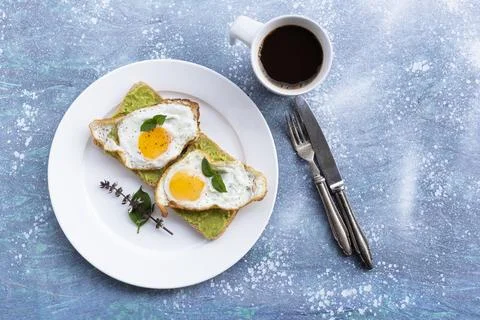 Breakfast food fried egg on bread avocado spread and coffee on blue wood tabl Stock Photos