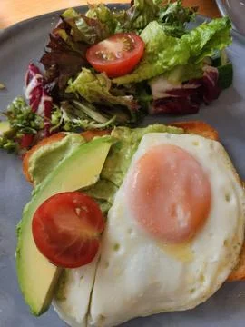 Breakfast with fried egg, avocado, tomato and salad on plate Stock Photos