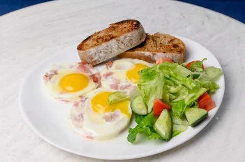 Breakfast of fried eggs with bacon, mixed salad and toasted bread Stock Photos