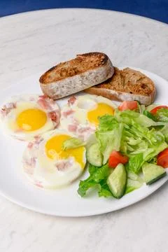 Breakfast of fried eggs with bacon, mixed salad and toasted bread Stock Photos