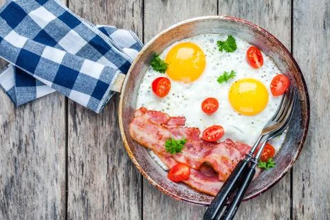 Breakfast with fried eggs, bacon, tomatoes and parsley Stock Photos