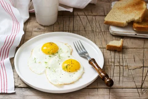 Breakfast of fried eggs, bread toasts and coffee on a wooden table. Rustic st Stock Photos