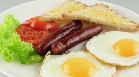 Breakfast with fried eggs, sausages, toasts and tomatoes on white plate Stock Footage 56427947