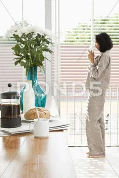 Breakfast on a kitchen counter and a women in pajamas drinking coffee Stock Photos
