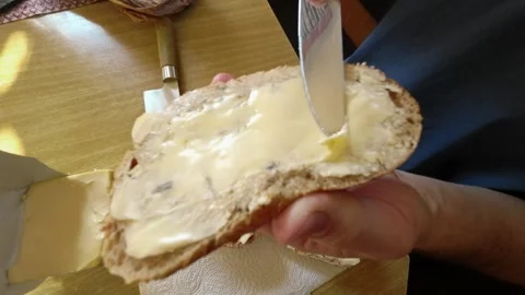 Breakfast. Man spreading butter on bread close-up sitting in cozy kitchen. Stock Footage 285525867