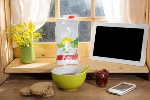 Breakfast with milk, bread, tablet and phone, on the edge of a window Foto stock