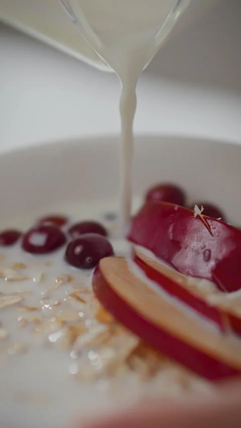 Breakfast moment as homemaker adds milk to oatmeal with apple and grapes in Stock Footage 331535872