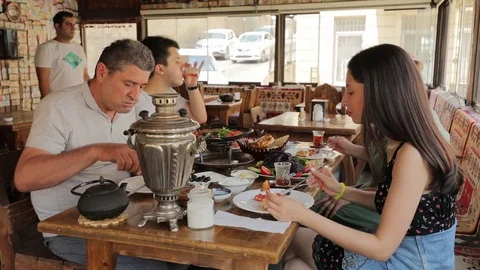 Breakfast in oriental cafe. On the table are samovar and snacks. Everyone eats Stock Footage 123543187