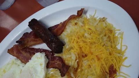 Breakfast over easy eggs sausage bacon hash browns with cheese close up Stock Footage 214149725