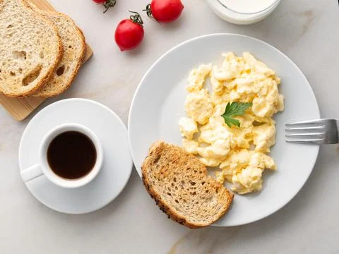 Breakfast with pan-fried scrambled eggs, cup of coffee, tomatoes on white stone Stock Photos