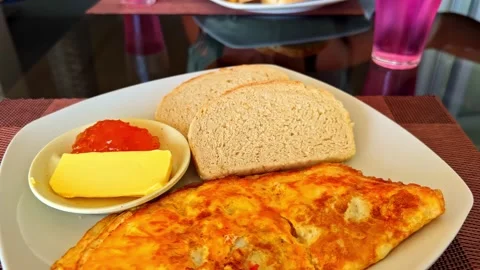Breakfast plate with a golden omelette, sliced bread, butter, and jam on a Stock Footage 334045997