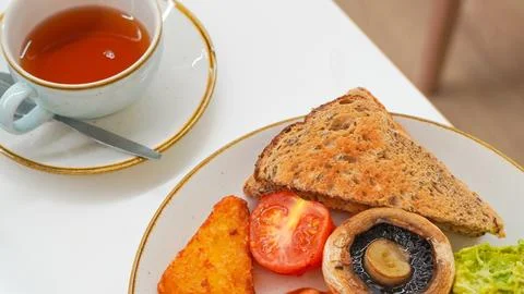 Breakfast plate with toast, tomatoes, mushrooms, and tea on white table Stock Photos