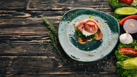 Breakfast. Poached egg, bacon on lettuce made from toast. On a black wooden b Stock Photos