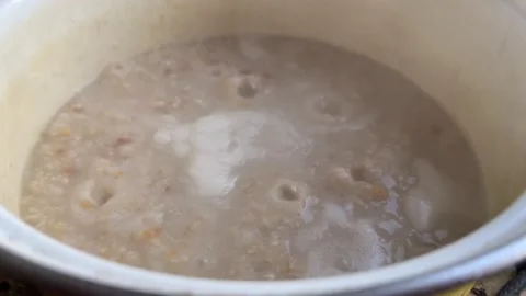 Breakfast preparation process. Oatmeal is cooked in an enamel white pan Stock Footage 254131180
