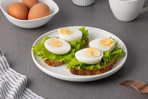 Breakfast scene with boiled eggs, lettuce on bread, tea, and eggs on a gray.. Stock Photos